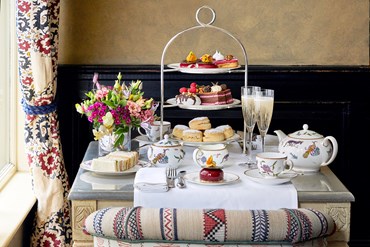 Champagne afternoon tea displayed on a table in Brasserie Max at the Covent Garden Hotel.  The fine bone china is Mythical Creatures by Kit Kemp for Wedgwood along side a 3 tier cake stand, sandwiches and scones.
