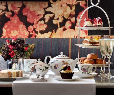 Champagne afternoon tea displayed on a table in Refuel restaurant at The Soho Hotel.  The fine bone china is Mythical Creatures by Kit Kemp for Wedgwood along side a 3 tier cake stand, sandwiches and scones.