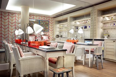 A nail bar with two tables and chairs. The far wall is floor to ceiling mirrors and in the reflection you can see an orange and pink patterned wall covering