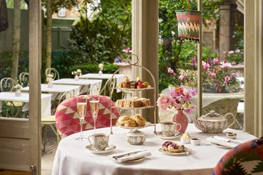 Champagne afternoon tea displayed on a table in the Orangery looking on to the garden at Number Sixteen hotel.  The fine bone china is Mythical Creatures by Kit Kemp for Wedgwood along side a 3 tier cake stand, sandwiches and scones.