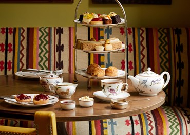 Champagne afternoon tea displayed on a table in The Potting Shed restaurant at the Dorset Square Hotel.  The fine bone china is Mythical Creatures by Kit Kemp for Wedgwood along side a 3 tier cake stand, sandwiches and scones.