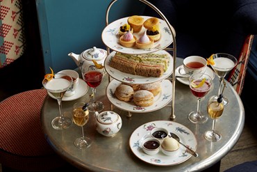 Champagne afternoon tea displayed on a table in Oscar restaurant at the Charlotte Street Hotel.  The fine bone china is Mythical Creatures by Kit Kemp for Wedgwood along side a 3 tier cake stand, sandwiches and scones.