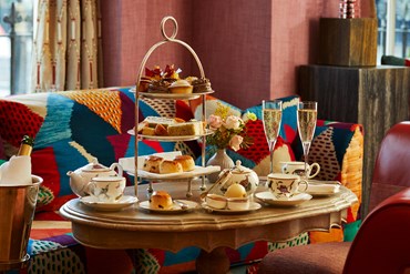 Champagne afternoon tea displayed on a table in Brumus restaurant at the Haymarket Hotel.  The fine bone china is Mythical Creatures by Kit Kemp for Wedgwood along side a 3 tier cake stand, sandwiches and scones.